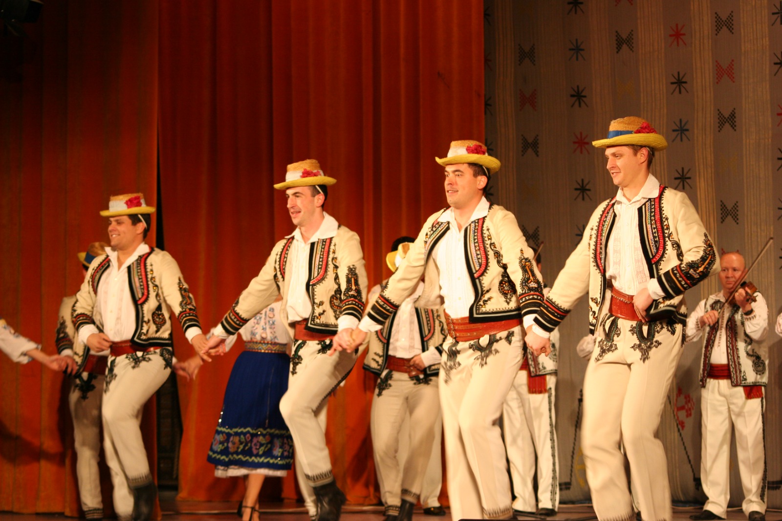 Dansatori ai Ansamblului Folcloric Tarabostes interpretând joc popular românesc pe scenă, în costume tradiționale autentice